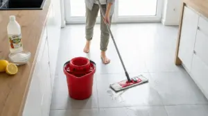 Persona mentre lava il pavimento di una cucina con mocio e secchio rosso