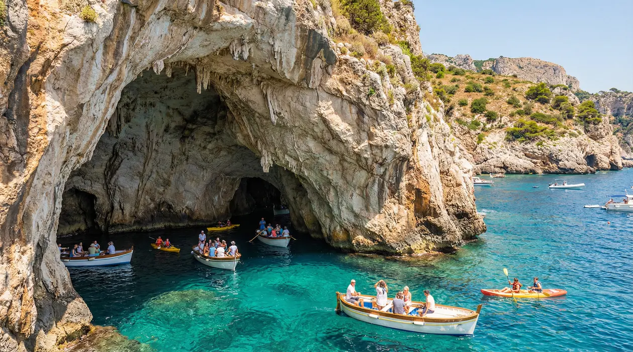 Barche con turisti davanti all'ingresso di una grotta marina su una costa rocciosa italiana