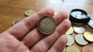 Moneta da 1 euro con il disegno dell'Uomo Vitruviano tenuta in mano, circondata da altre monete