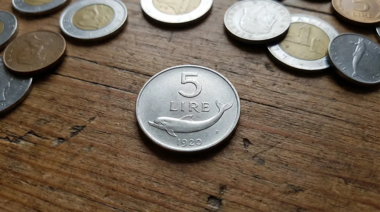 Una moneta da 5 lire con un delfino incisa su un tavolo di legno