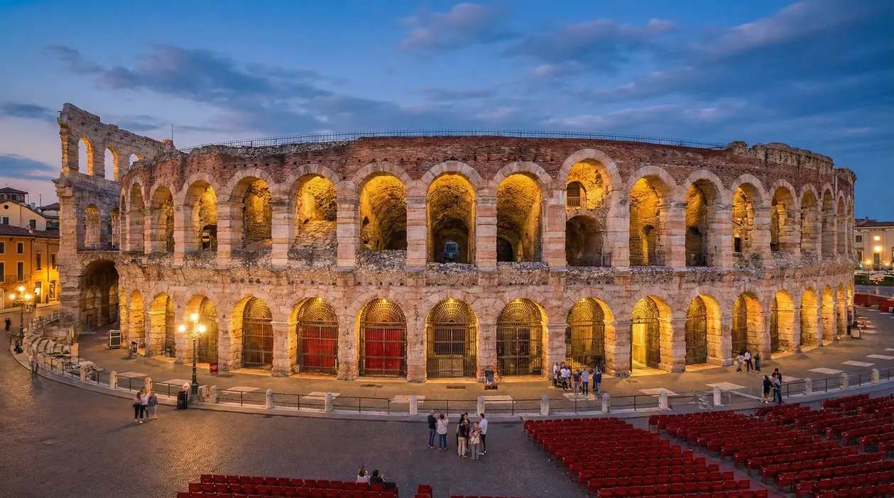 Arena di Verona illuminata al tramonto con alcune persone nella piazza davanti
